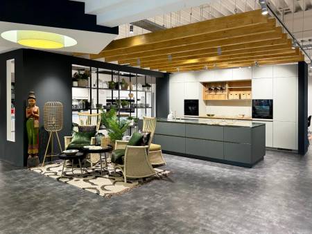 Modernes Küchendesign mit grünen Lounge-Sesseln, großer Statue und Pendelleuchte auf grauem Boden.