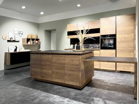 Elegante Küche mit Holzinsel und Schränken, Akzentbeleuchtung und dekorativen Elementen auf grauem Untergrund.