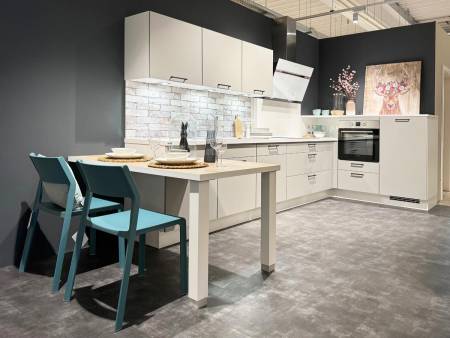 Schlichte weiße Küche mit Ziegelsteinrückwand, türkisfarbenen Stühlen und moderner Kunst auf grauem Boden.