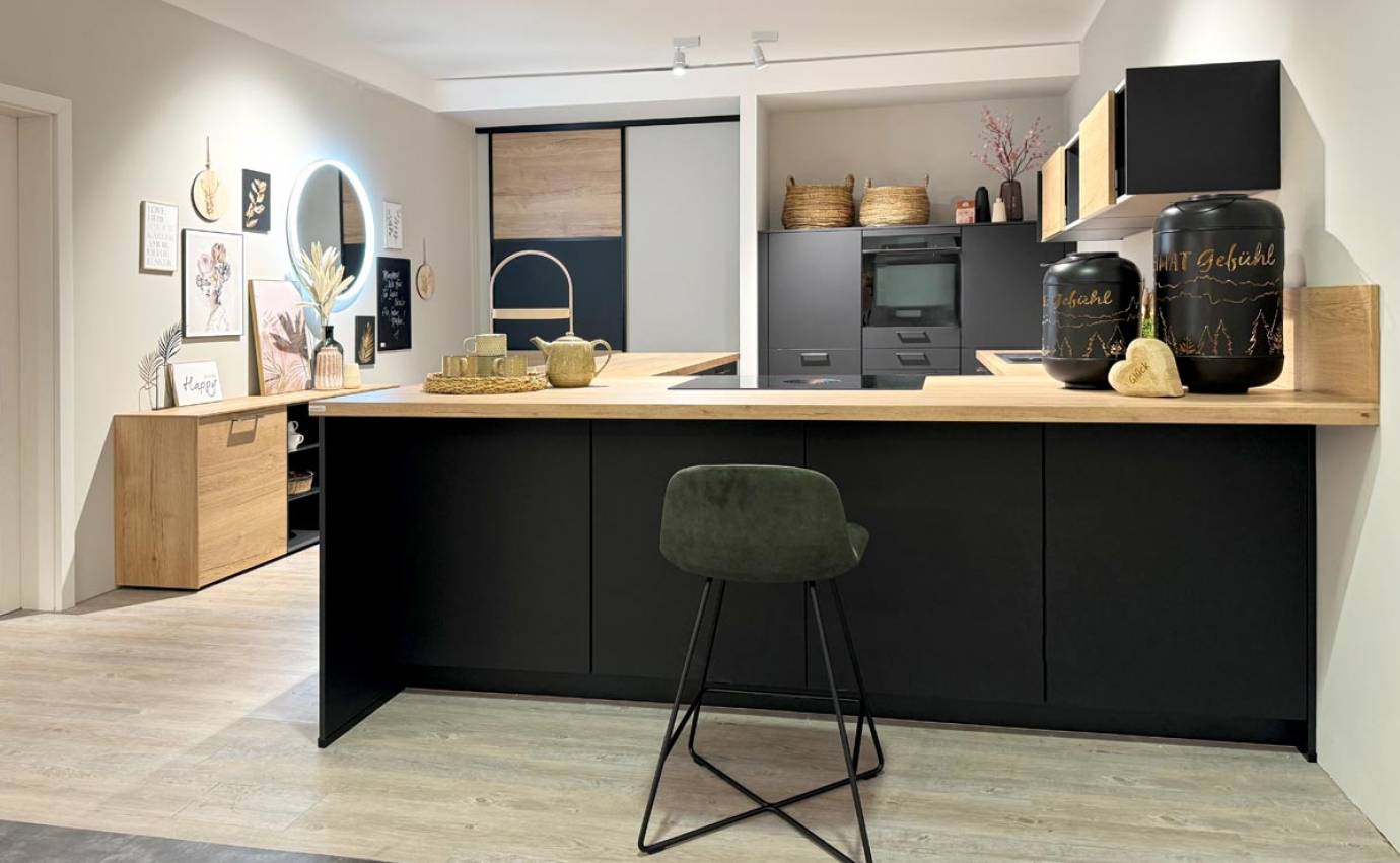 Kombinierter Küchen- und Wohnbereich mit schwarzen und Holzelementen, runden Wanddekorationen und Pflanzen auf hellem Holzboden.