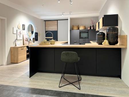 Kombinierter Küchen- und Wohnbereich mit schwarzen und Holzelementen, runden Wanddekorationen und Pflanzen auf hellem Holzboden.