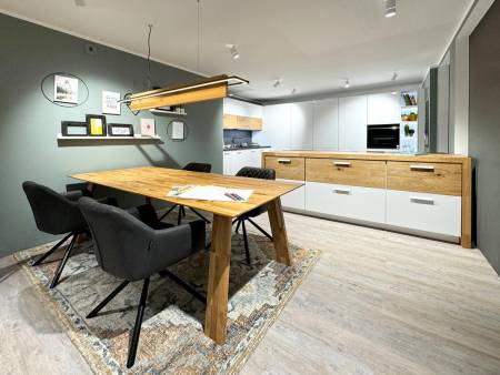 Offener Küchen- und Essbereich mit Holztisch, schwarzen Stühlen und weißen Schränken, Beleuchtung oberhalb des Tisches.