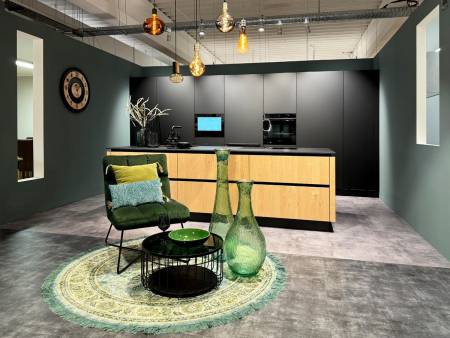 Gemütliche Sitzecke mit grünem Sessel, runder Teppich und Kücheninsel mit Holzelementen auf grauem Boden.