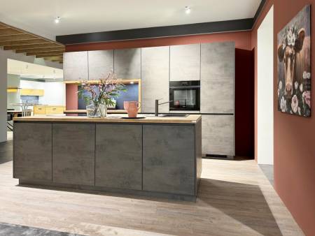 Moderne Kücheninsel mit Betonoptik vor einer Kombination aus hochglänzenden und matten Schränken, unterstrichen von einer warmen Holzdecke und einem großen Gemälde an einer terrakottafarbenen Wand.