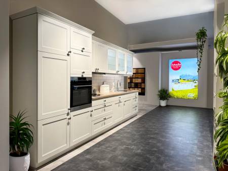 raditionelle weiße Küche mit klassischem Design und modernen Geräten, belebende Pflanzen und großes Fensterplakat auf grauem Boden.