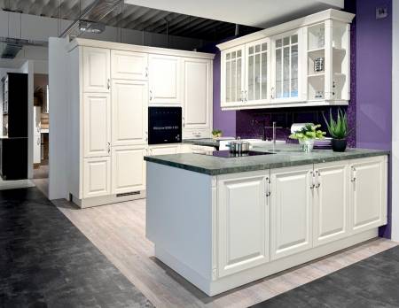 Klassische cremefarbene Küche mit Insel, eingelassener Beleuchtung und Glasschränken an einer lila Wand.