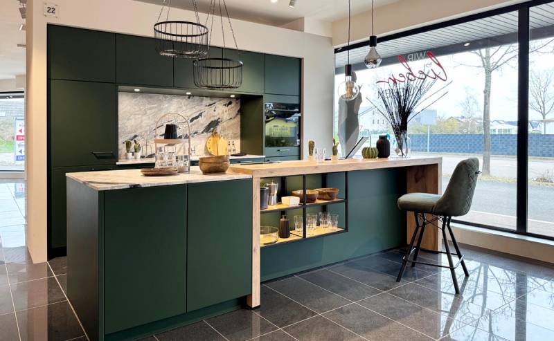 Moderne grüne Küche mit zentraler Insel und Marmoroptik, umgeben von stilvollen Hängelampen und Glasfronten.