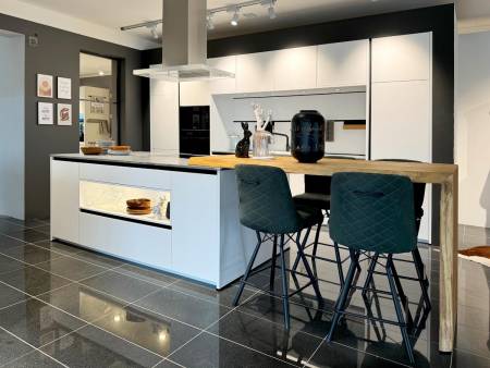 Helles Küchendesign mit weißer Einrichtung, schwarzen Hochstühlen und Holzdetails, neben einem modernen Esstisch.