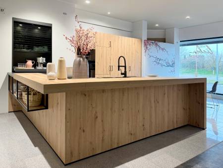 Hellholzige Kücheninsel im skandinavischen Design mit schwarzer Armatur und dekorativen Vasen auf einem offenen Regal in einem lichtdurchfluteten Raum.