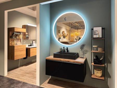 Stilvolles Badezimmerdesign mit rundem, beleuchtetem Spiegel über einem dunklen Waschtisch und hölzernen Dekorelementen.