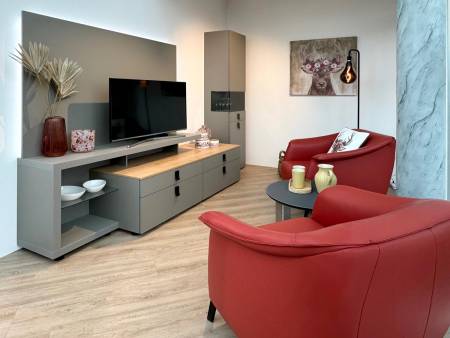 Gemütlicher Wohnraum mit grauer TV-Wand, hölzerner Ablage, roten Sesseln und dekorativer Hirsch-Kunst an der Wand.